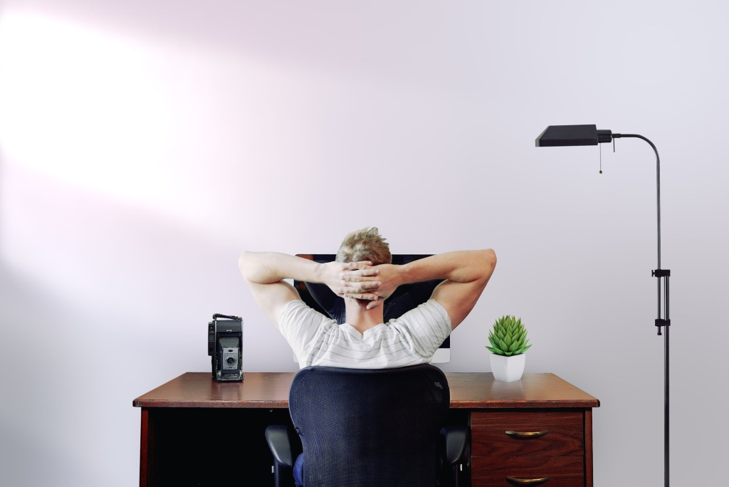 A man is sitting at a desk with his hands behind his head.